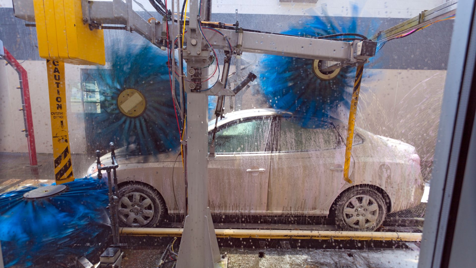 Automated car wash with robotic arms cleaning a white sedan
