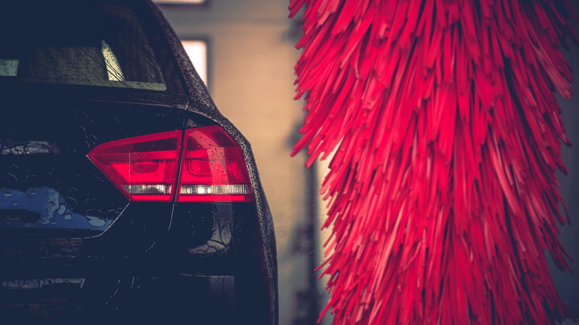 Black car with wet surface next to bright red car wash brushes