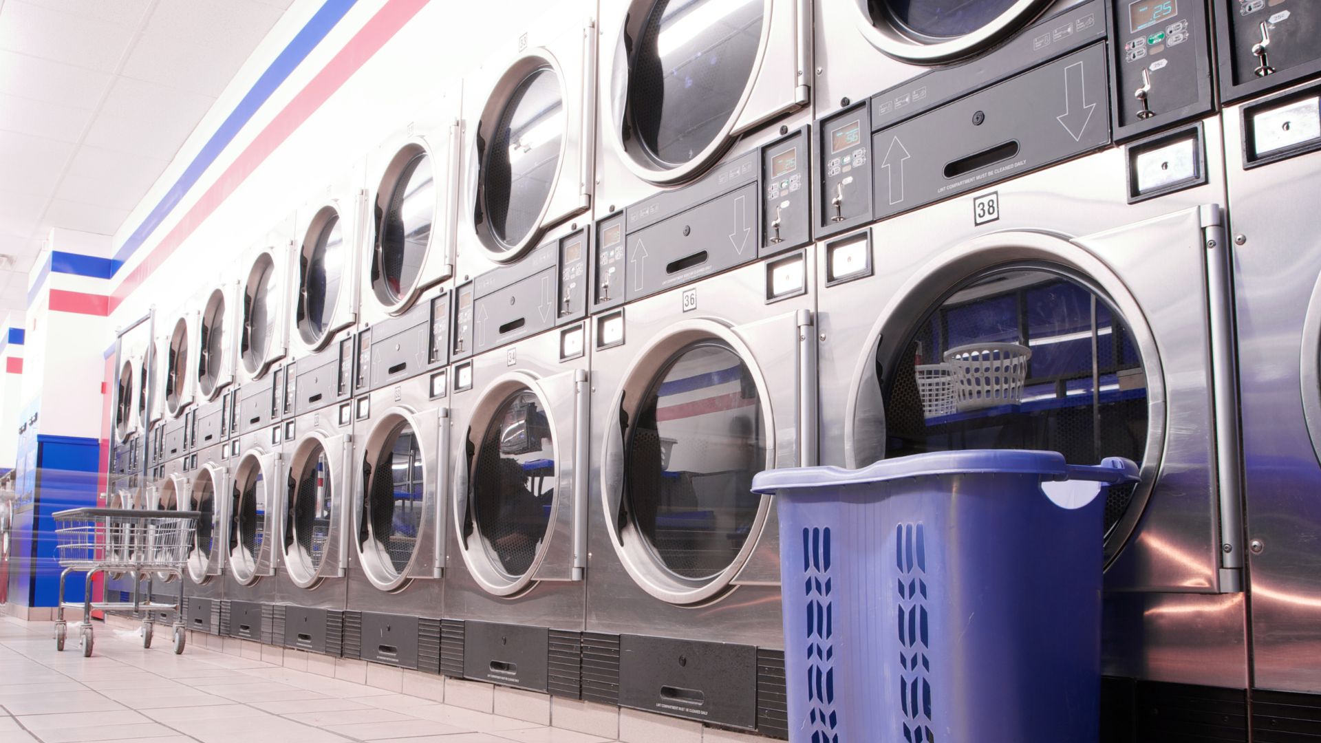 Row of industrial washing machines in a clean laundromat with blue basket