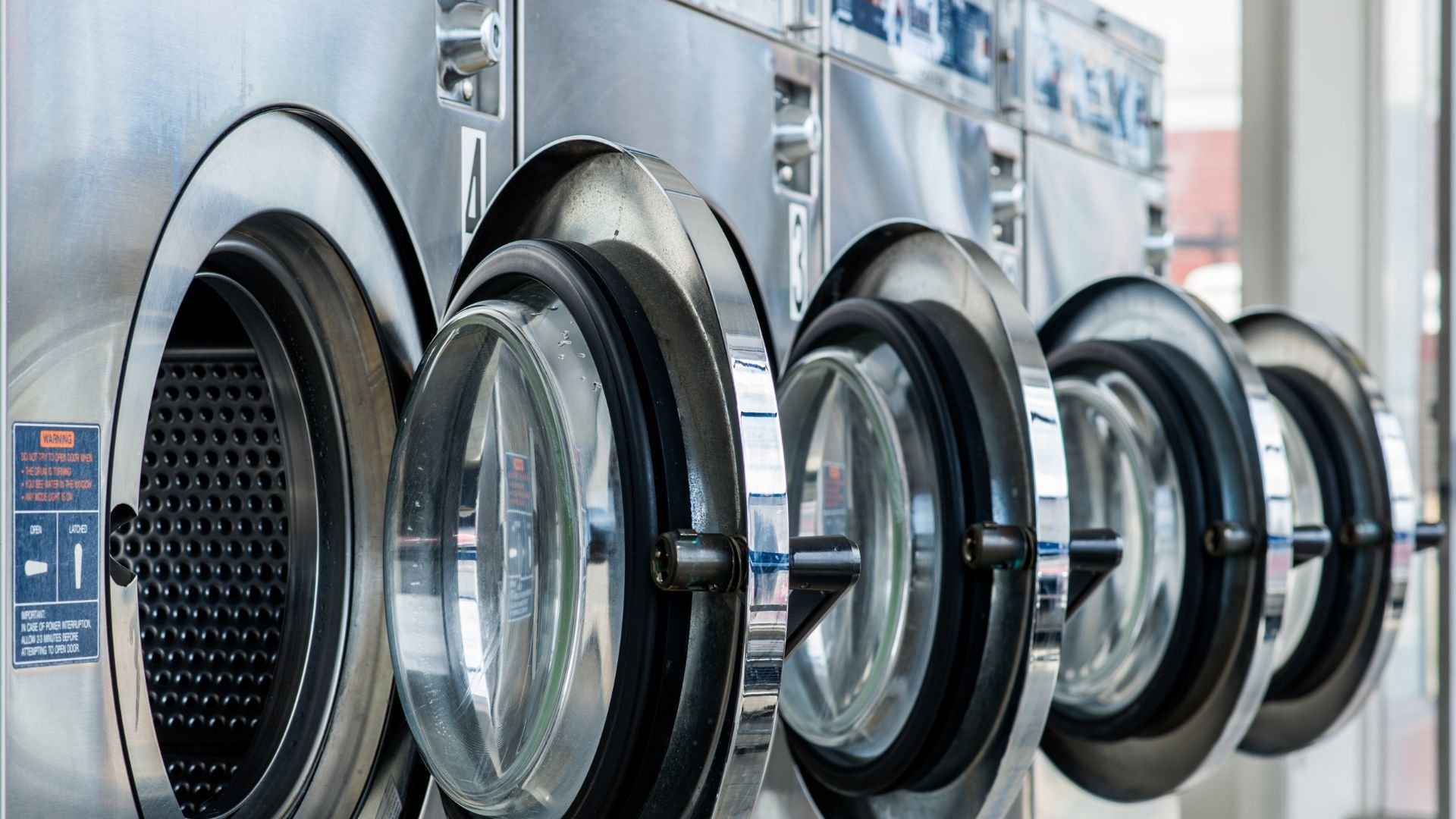 Row of industrial washing machines in a laundromat, ready for use