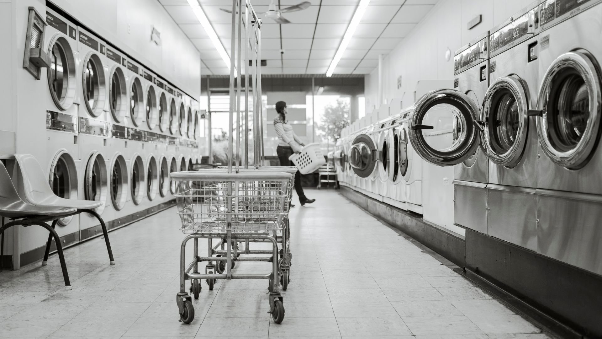 Rows of washing machines with laundry cart in empty black and white laundromat