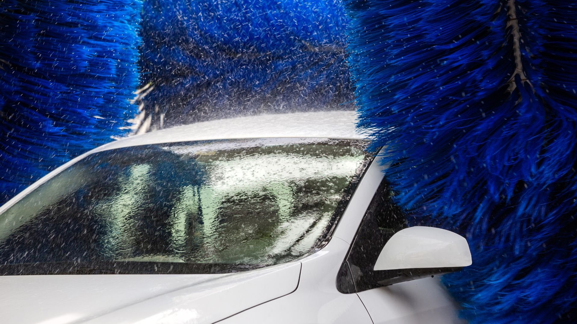 White car going through automated car wash with blue spinning brushes