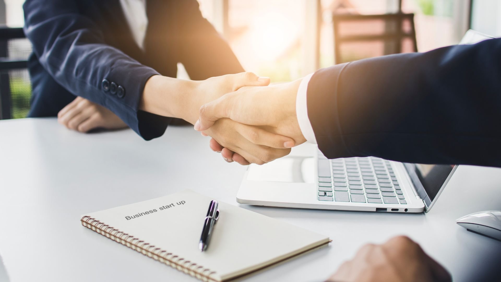 Business professionals shaking hands after meeting with laptop and notebook